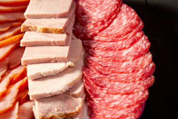 A plate of meat and cheese with a red slice of pepperoni. The plate is on a black background