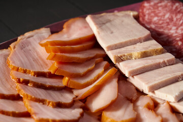 A plate with sliced meat, including sausage, ham, pork, and smoked meat. A detailed view