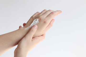 Hand cream. Close-up of young woman's hands with moisturizing cream. Skin care. Woman applying cream on her hands, light background. Healthy skin. Cosmetology. Daily routine