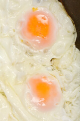 A close-up of two fried eggs with set whites and orange yolks