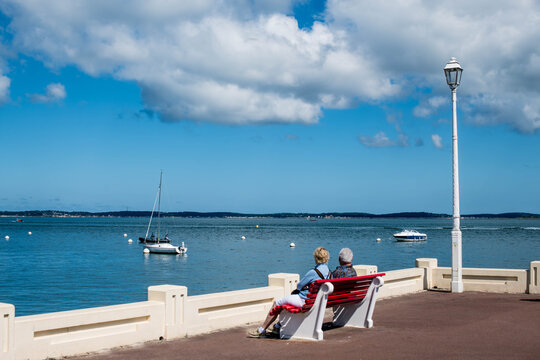 Senior couple sitting on a bench facing the Arcachon Bay and its Winter Town