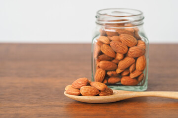 Almonds in wooden spoon on table background. Almonds in glass jar. Selective focus.