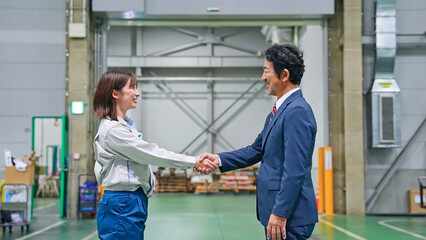 工場の中で握手する男性ビジネスパーソンと女性作業員