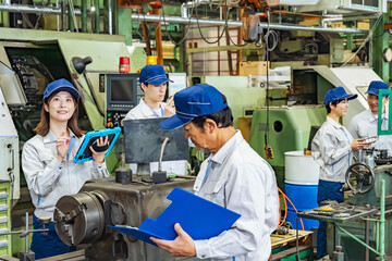 タブレットPCを持って機械を点検する作業員グループ