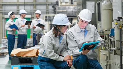 タブレットを持って工場機械を点検する男女作業員