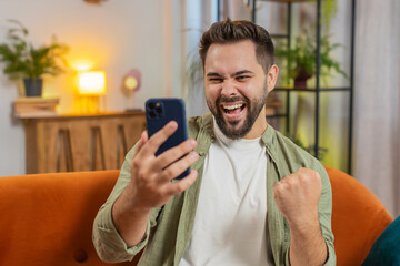 Happy young man using smartphone typing browsing saying yes, celebrating success victory, winning...