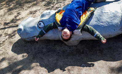 SHOTLISTtravel, boy 9 years old lying on a decorative hippopotamus, upside down, spring park, arms...