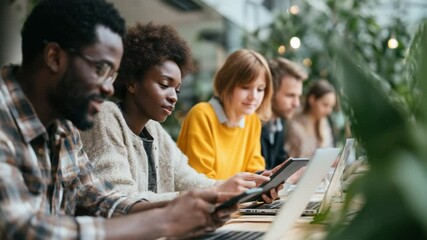 Teamwork and Technology: A diverse team of young professionals collaborates on a project, using laptops and tablets in a modern, collaborative workspace. The image emphasizes teamwork, technology. - Powered by Adobe