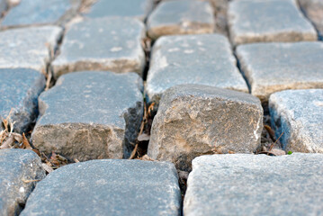 Misaligned cobblestone sticking out from cracked street paving in the city, highlighting infrastructure aging and the urgent necessity for repair and maintenance. Need for cobblestone road repair