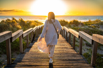 Algarve coast in Portugal. Middle aged woman walking down stairs overlooking beautiful beach on sunset. Back view