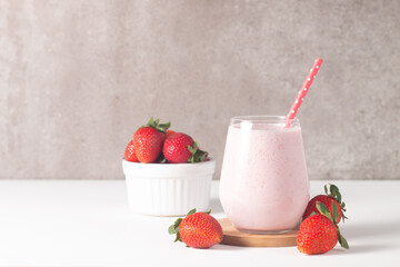 Glass of fresh strawberry milkshake, smoothie and fresh strawberries on white and wooden...