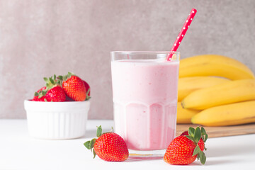 Glass of fresh strawberry milkshake, smoothie and fresh strawberries on white and wooden...