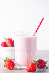 Glass of fresh strawberry milkshake, smoothie and fresh strawberries on white and wooden...