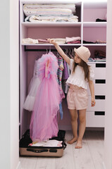 A little girl of European appearance puts things in a suitcase in a dressing room. Preparation,...