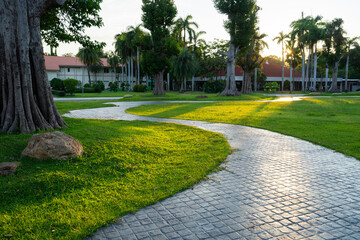 Winding stone path leads through lush green park with tall trees and building in background
