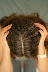 Naklejka premium Close-up view from above of a woman touching her scalp and showing gray roots. Beauty in aging, self-acceptance, and gentle hair care. Natural transformation, soft light, healthy texture.