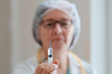 Close-up view of a medical professional in a white uniform holding a syringe. Focus is on the syringe filled with medication. Symbol of healthcare, prevention, and medical responsibility.