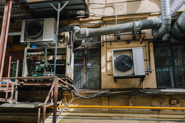 building with a large air conditioner on the wall. The building is old, and there are many pipes...