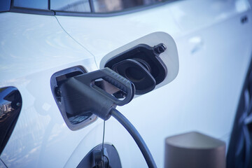 A closeup view of a electric car battery power charger plug in a tank cap of a white car
