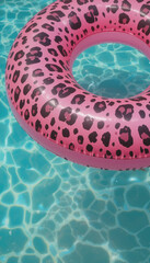 Pink leopard print pool float resting in clear blue water on a sunny day