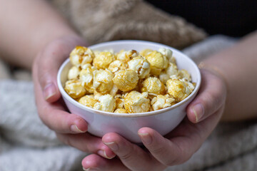Close up asian woman hand reeaxing with a bowl of sweet caramel popcorn. Perfect for cozy movie nights at home