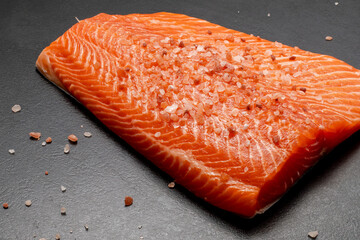 Fresh raw salmon or trout fillet sprinkled with coarse salt. Black background. Healthy seafood food.