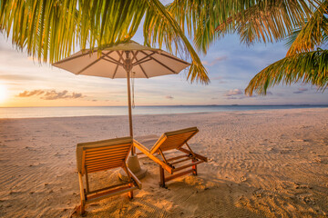 Closeup sunset sky sea sand beach chairs umbrella and palm leaves. Dreamy tropical vacation travel. Luxury seaside escape, romantic coastal view. Summer relaxation best exotic travel paradise getaways