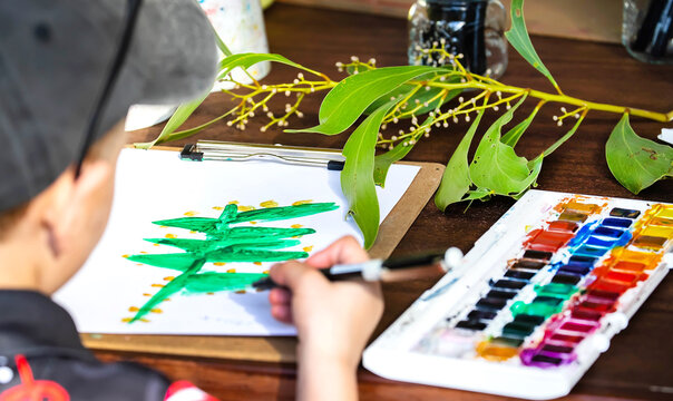 Child painting eucalyptus leaf with watercolors during nature art activity