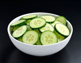 a bowl of sliced cucumber isolated on a black background 