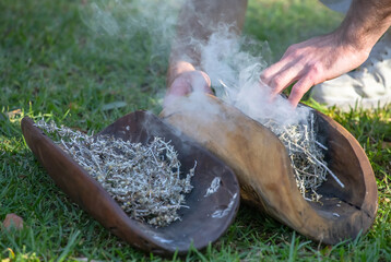 Australian Aboriginal smoking ceremony, human hands and wooden dish with a smoke of burning tree branches, the ritual rite at the community event, symbol of joining to the indigenous culture