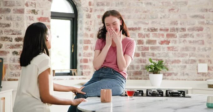 Diverse female friends gathering at marble kitchen island laughing, revealing engagement ring