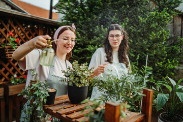 Two female friends or sisters taking care of plants with water can and mister