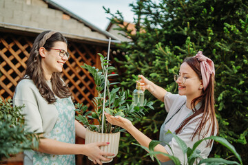 Two female friends or sisters taking care of plants with water can and mister