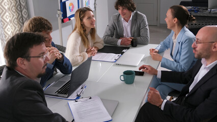 A team of young business people are chatting at a table in a conference room. They are all dressed...