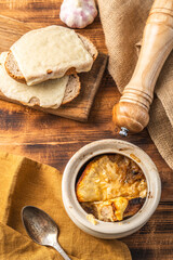 Fototapeta premium Onion soup in a pot according to a traditional French recipe with a cheese crust, on a wooden background with toasted bread and cheese.