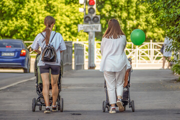 Women walk along the sidewalk with baby strollers on a summer day