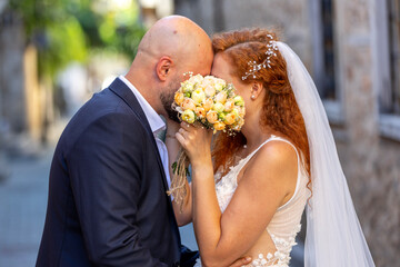 Wedding couple kissing and hugging each other on their wedding day hiding faces behind a bouquet