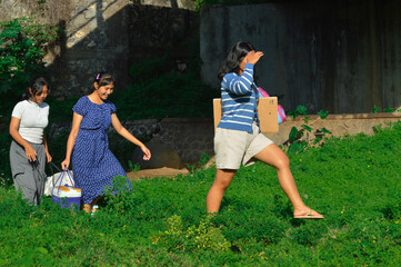 Girls walk through uneven grassy land, smiling as they carry supplies in warm sunlight
