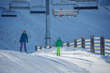 Adult woman and child ski under chairlift on sunlit snowy slope