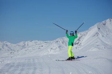 Skier in neon green jacket lifts poles overhead on sunlit slope