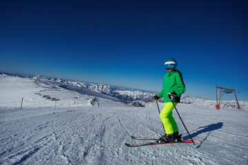 Skier in green jacket stands upright on skis overlooking valley