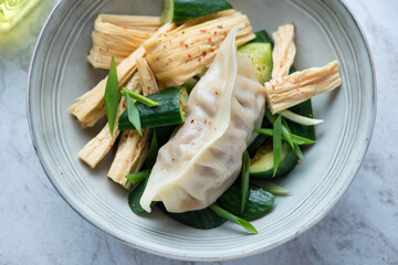 Grey plate with smashed cucumber salad, tofu skin and steamed pork dumpling, horizontal shot, middle closeup, selective focus