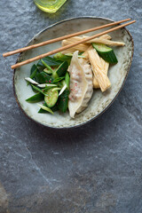 Bowl with smashed cucumber salad, yuba and pork dumpling on a dark-grey granite background, vertical shot with space, top view
