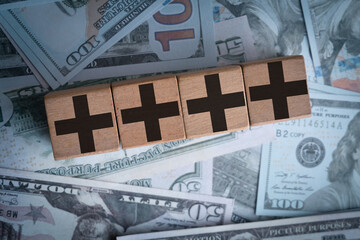 Wooden blocks with plus signs placed on a background of US dollar bills. Concept of financial...