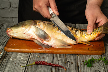 A person skillfully fillets a fresh fish on a wooden cutting board in a rustic kitchen. The scene...