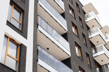 Modern residential apartment building. Minimalist contemporary facade. New real estate in city. Architecture with glass balconies and dark brick wall. Urban housing concept. Stylish city apartments.