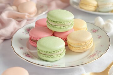 Fototapeta premium Pastel Macarons Stacked on Floral Plate with Soft Pink Fabric Backdrop