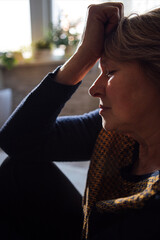 Close-up of an elderly woman suffering from a headache. A mature lady is sitting on the floor and holding her forehead with her hand.