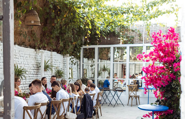 A festive banquet outdoors in the garden. Elegant guests at the tables. Rustic stylish interior. Grapes on the walls and flowering trees.