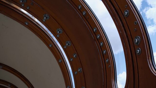Close-up of steampunk airship window frames with bolts and curved wood against blue sky

